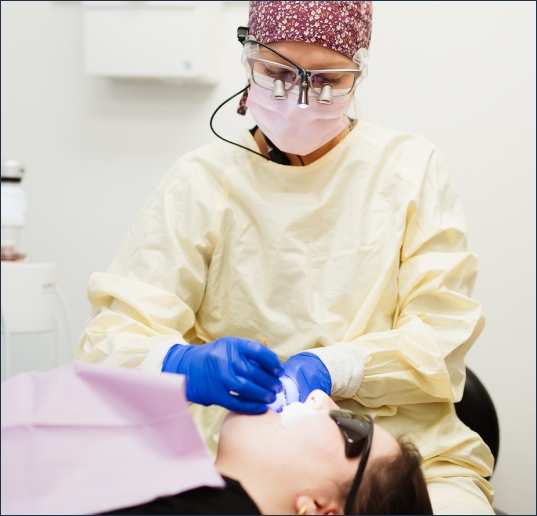 A female dentist examines the teeth of her patient using dental tools